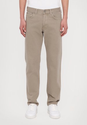 Beige rechte spijkerbroek gedragen met een wit shirt en witte sneakers, getoond van taille tot voeten tegen een effen achtergrond.