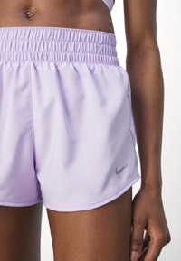 Pantalones deportivos de color púrpura claro con cinturilla elástica fruncida y un pequeño logotipo gris de Nike en el lado inferior derecho. Textura lisa.