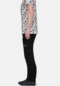 Czarne spodnie outdoorowe o slim fit, z kieszeniami na zamek i wzmocnionymi szwami. W połączeniu z białą koszulką z grafiką i czarnymi butami.