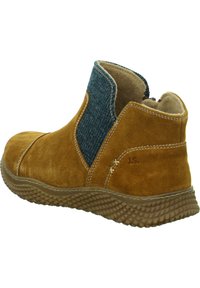 Beige Wildleder-Stiefeletten mit einem strukturierten blauen Elastikeinsatz, ausgestattet mit einer Gummisohle und dekorativen Nähten an der Seite.