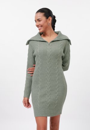 Knit dress in soft green with cable pattern, zip neckline, and wide collar. Long sleeves, fitted silhouette, and ribbed hem detail.