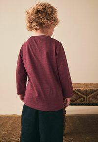 Pikad varrukad maroon värvi särk, mis on valmistatud pehmest kangast, ümmarguse kaelusega ja veidi kõveriku hemiga; kantud tumedate, laiemate pükstega.