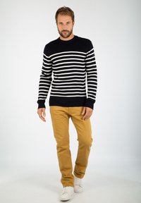 Maglione a righe blu navy e bianche con scollatura rotonda e dettaglio a bottoni su una spalla, abbinato a pantaloni color senape e sneaker bianche.