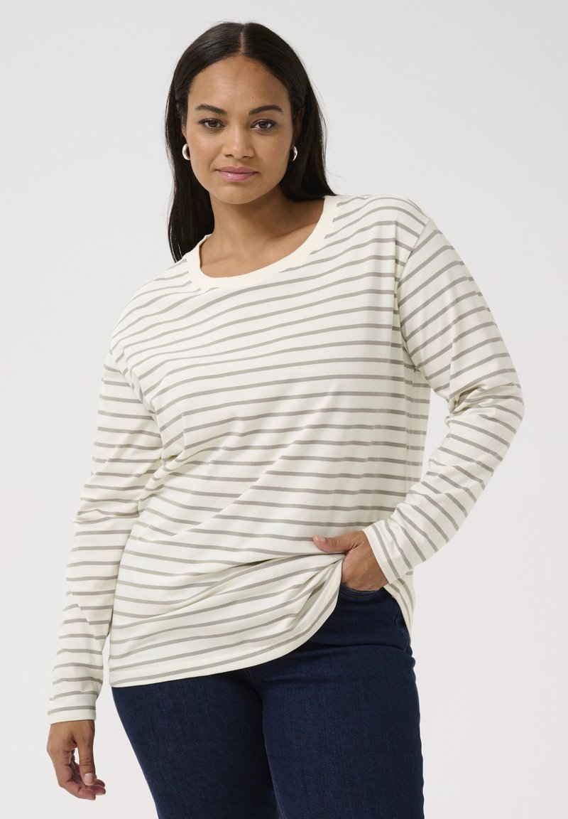 Striped long-sleeve shirt in cream and light gray, featuring a round neckline and soft fabric. Paired with dark jeans, showing a relaxed fit.