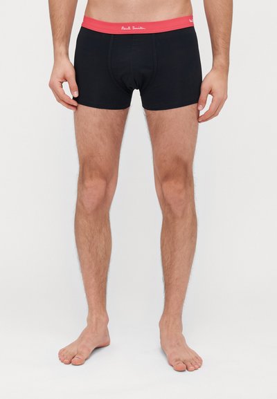Boxers noirs pour hommes avec une ceinture élastique rouge portant "Paul Smith" en écriture blanche. Réalisés en tissu doux, offrant un ajustement confortable.