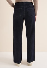 Tummansiniset denimpöksyt suorilla lahkeilla, joissa on kaksi takataskua ja tikattu vyötärönauha, yhdistettynä vaaleanvärisiin tennareihin.