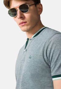 Szary polo z zielonymi akcentami i trzema guzikami. W zestawie z okrągłymi okularami przeciwsłonecznymi, prezentującymi nowoczesny design i doskonałą teksturę.