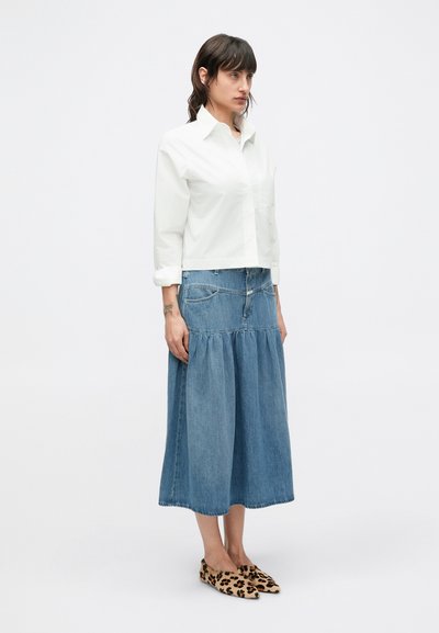Biela krátka košeľa so špicatým golierom, skombinovaná s modrou džínsovou maxi sukňou s vrstvami a topánkami na sklz s leopardím vzorom.