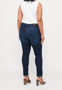 Dark blue skinny jeans with a mid-rise waist, subtle fading, rear patch pockets, and frayed hem, paired with leopard print high-heeled sandals.
