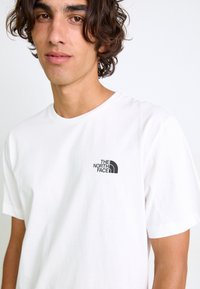 Tricou alb din bumbac, cu un logo imprimat negru al "The North Face" pe partea stângă a pieptului. Mâneci scurte și gât rotund.