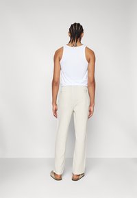 Witte tanktop, beige gestructureerde broek, rechte pijpen, twee achterzakken en platte sandalen. Neutrale kleuren, casual ontwerp, minimale details.
