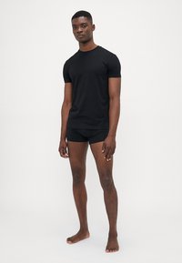 Schwarzes T-Shirt mit kurzen Ärmeln aus atmungsaktivem Stoff, kombiniert mit schwarzen engen Shorts. Glatte Textur und schlichtes Design, minimalistischer Stil.