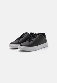 Adidași din piele neagră cu talpă din cauciuc alb. Textură netedă, vârf rotund, șireturi în față și un branding subtil auriu pe lateral.