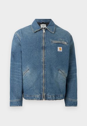 Μπλε τζιν μπουφάν με μπροστινό φερμουάρ, δύο διαγώνιες κάτω τσέπες, μια τσέπη στο στήθος με φερμουάρ και ένα τετράγωνο λογότυπο Carhartt στο στήθος.