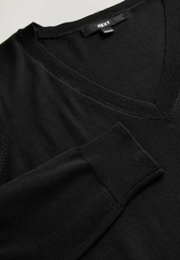 Crni pulover s v-neck izrezom i dugim rukavima, s glatkom teksturom i rebrastim ovratnikom, položen ravno na svijetloj podlozi.