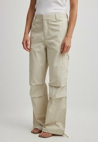 Beige cargo-housut, joissa on rento istuvuus, vetoketjulliset lahkeet, suuret taskut ja puuvillasekoitemateriaali, sopii rentoon pukeutumiseen.