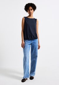 Mörkblå ärmlös topp med rund halsringning, samlad vid midjan, tillsammans med ljusblå vida jeans och svarta platta skor.