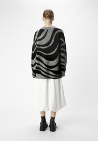 Løs pasform sort og grå sweater med bølgede striber, lavet af tekstureret materiale. Båret over en hvid nederdel, parret med sorte sko og sokker.