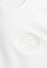 Weißes, leichtes Stoff-T-Shirt mit rundem Halsausschnitt, versehen mit einem strukturierten, erhabenen runden Logo auf der Brust.