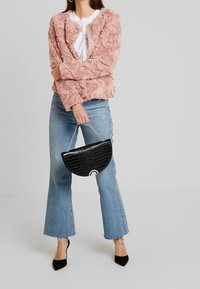Růžová bunda z umělé kožešiny s texturovaným vzorem, doplněná modrými zvonovými džínami a černou polokruhovou kabelkou se stříbrným řetízkovým detailem.