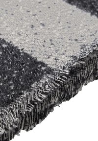 Wollteppich mit einem karierter Muster in Grau und Schwarz. Texturierte Oberfläche mit ausgefransten Kanten und variierenden Florhöhen.