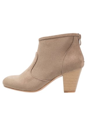 Beige suède enkellaars met zijstiksels, gestapelde blokhak, afgeronde neus en ritssluiting aan de achterkant.