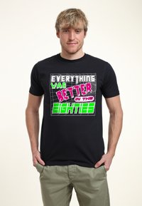 Camiseta de algodón negra con texto impreso colorido que dice "TODO era MEJOR en los OCHENTA" en fuentes negritas y de estilo retro.