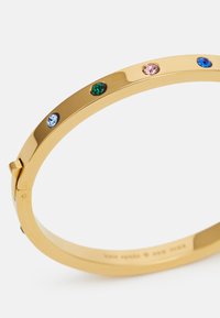 Bracciale rigido in tono dorato con finitura liscia, caratterizzato da cinque gemme colorate: verde, azzurro chiaro, rosa, blu scuro e trasparente.