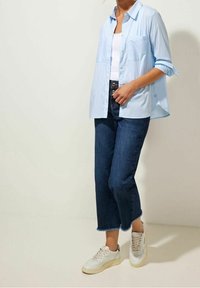 Ljusblå randig skjorta med uppvikta ärmar, två framfickor, kombinerad med mörkblå caprijeans och vita sneakers.