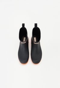 Ghete negre din cauciuc până la gleznă, cu un finisaj neted, având o talpă exterioară texturată de culoare portocalie și accesorii pentru a le putea îmbrăca ușor pe fiecare parte.