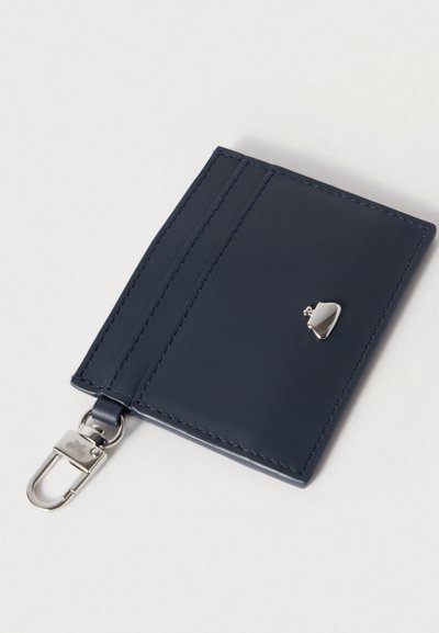 Τζιν μπλε δερμάτινη θήκη καρτών με κομψό σχέδιο, που διαθέτει δύο θήκες για κάρτες, ασημένιο κούμπωμα και μικρό ασημένιο έμβλημα στο μπροστινό μέρος.