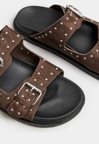 Sandali in suede marrone con borchie argentate, cinturini regolabili doppi e una suola nera spessa. Presentano una punta aperta e un design con ritagli.