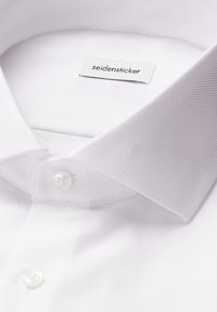 Camicia bianca con un delicato motivo a spina di pesce, bottoni perla e etichetta del marchio "Seidensticker" all'interno del colletto.