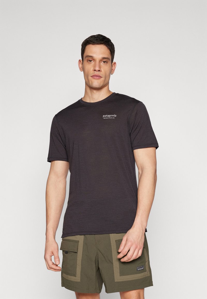 T-shirt grigio scuro a maniche corte con collo rotondo e logo bianco "Patagonia" sul petto sinistro. Indossato con pantaloni cargo verdi oliva.