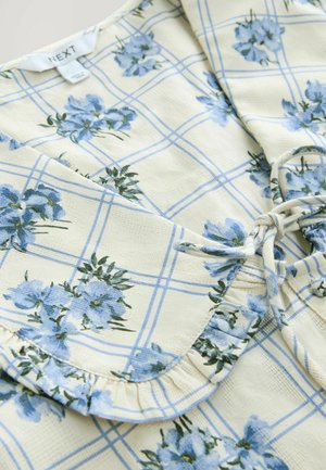Bluse mit floralem Muster aus strukturiertem Stoff. Sie hat blaue Blumen auf einem cremefarbenen Karomuster, mit einem Rüschensaum und einem Bindeband.