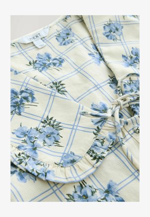 Floral-patterned blouse made of textured fabric. Features blue flowers on a cream grid background, with a ruffled collar and tie detail.