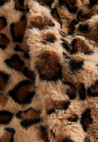 Leopardprint imiteret pels med en blød, fluffy tekstur i nuancer af lys brun, mørk brun og sorte mærker. Nærbillede fremhæver detaljerne.