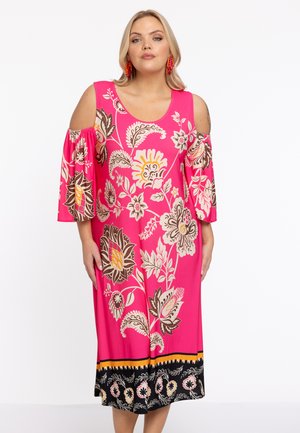 Robe florale rose avec des manches dénudées, ornée de grandes fleurs brunes et jaunes, avec un ourlet à motifs noirs et une coupe décontractée.