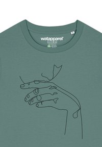 Grünes T-Shirt mit einer durchgehenden Linienstudie einer Hand, die einen kleinen Gegenstand hält. Es hat eine glatte Textur und einen Rundhalsausschnitt.