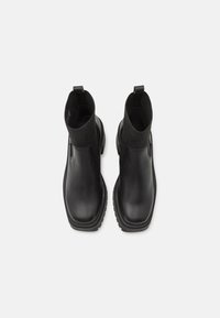 Musta nahkainen nilkkurit, joissa on kiinteä pinta, joustavat sivupaneelit ja paksu pohja. Varustettu pienillä vetonarupisteillä, jotka helpottavat pukemista.