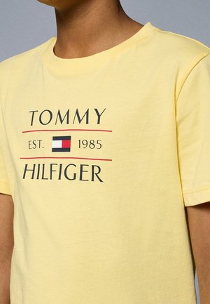 Geel katoenen T-shirt met het "TOMMY HILFIGER" logo in zwart met rode accenten, ronde halslijn en korte mouwen.