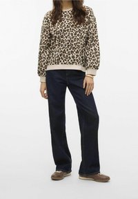 Sudadera de estampado de leopardo en beige y marrón, con puños y dobladillo acanalados, combinada con vaqueros de pierna ancha azul oscuro y zapatillas marrones.