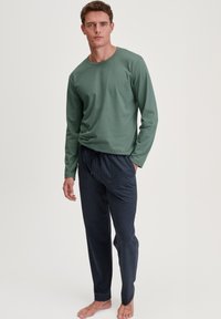 Lichtgroen shirt met lange mouwen, gecombineerd met marineblauwe gestreepte loungebroek met een trekkoord. Zachte stof, relaxte pasvorm en subtiele geometrische print.
