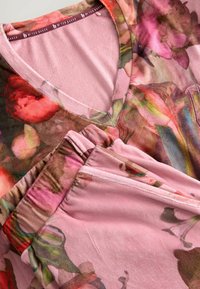 Tkanina w kwiatowy wzór w odcieniach różu i zieleni z miękkim, teksturowanym wykończeniem. Dekolt w serek z wygodnym, luźnym krojem.