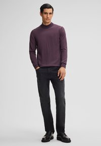 Maglione a collo alto viola scuro con tessuto testurizzato, indossato con jeans neri slim-fit e scarpe nere con lacci, mostrato in vista frontale.