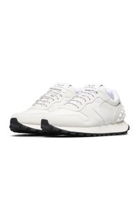 Scarpe da corsa in suede bianco con suole in gomma nera, caratterizzate da spessi borchie argento, lacci e marchio stampato sulla linguetta e sui lati.