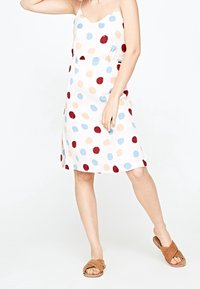 Vestido ligero sin mangas con lunares multicolores en rojo, azul y melocotón sobre un fondo blanco; cuenta con un ajuste relajado y aberturas laterales.