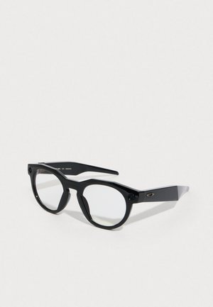 Black eyewear with an angular frame, featuring round lenses and textured temple arms. Notable hardware detailing on the sides.
