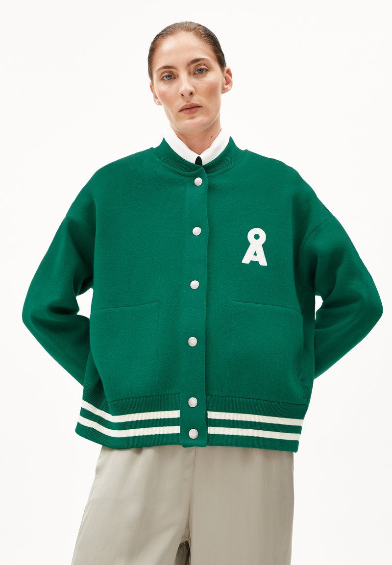 Veste en tricot verte avec un col rond, des boutonnières blanches, deux poches avant et des accents rayés au niveau de l'ourlet. Présente un logo blanc.