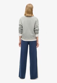 Grijze sweatshirt met afhangende schouders, gelaagd over een witte shirt, gecombineerd met brede marineblauwe broek met een contrasterende zijpaneel.